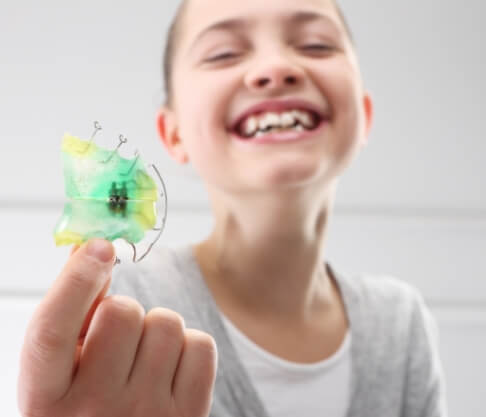 Child holding up an early interceptive orthodontic appliance